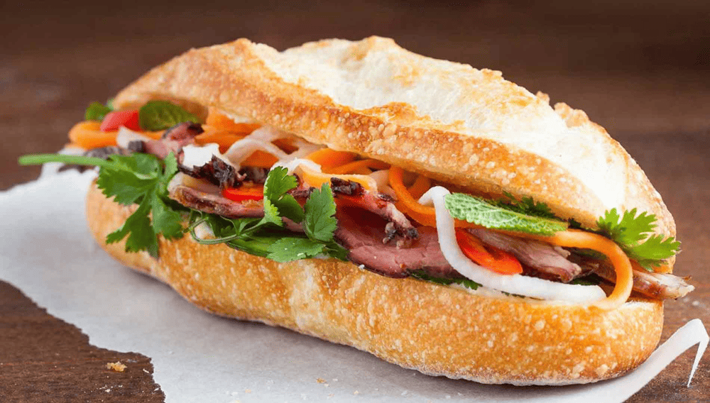 Golden crispy banh mi sandwich filled with colorful pickled vegetables and fresh cilantro